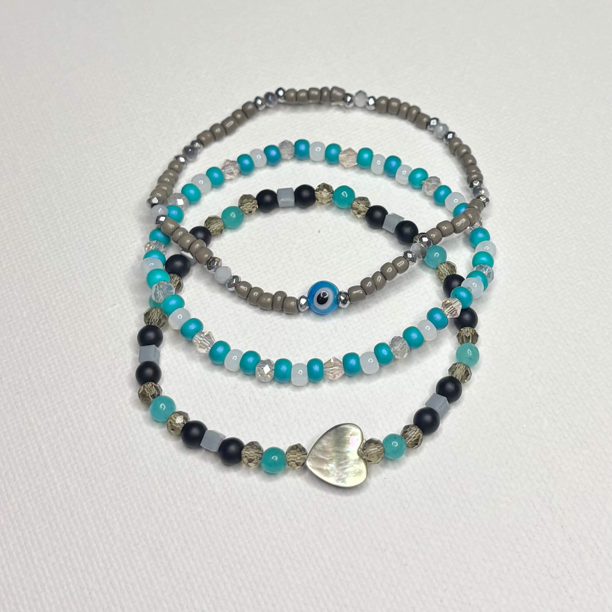 Three-piece beaded bracelet stack with shell heart and blue evil eye bead.