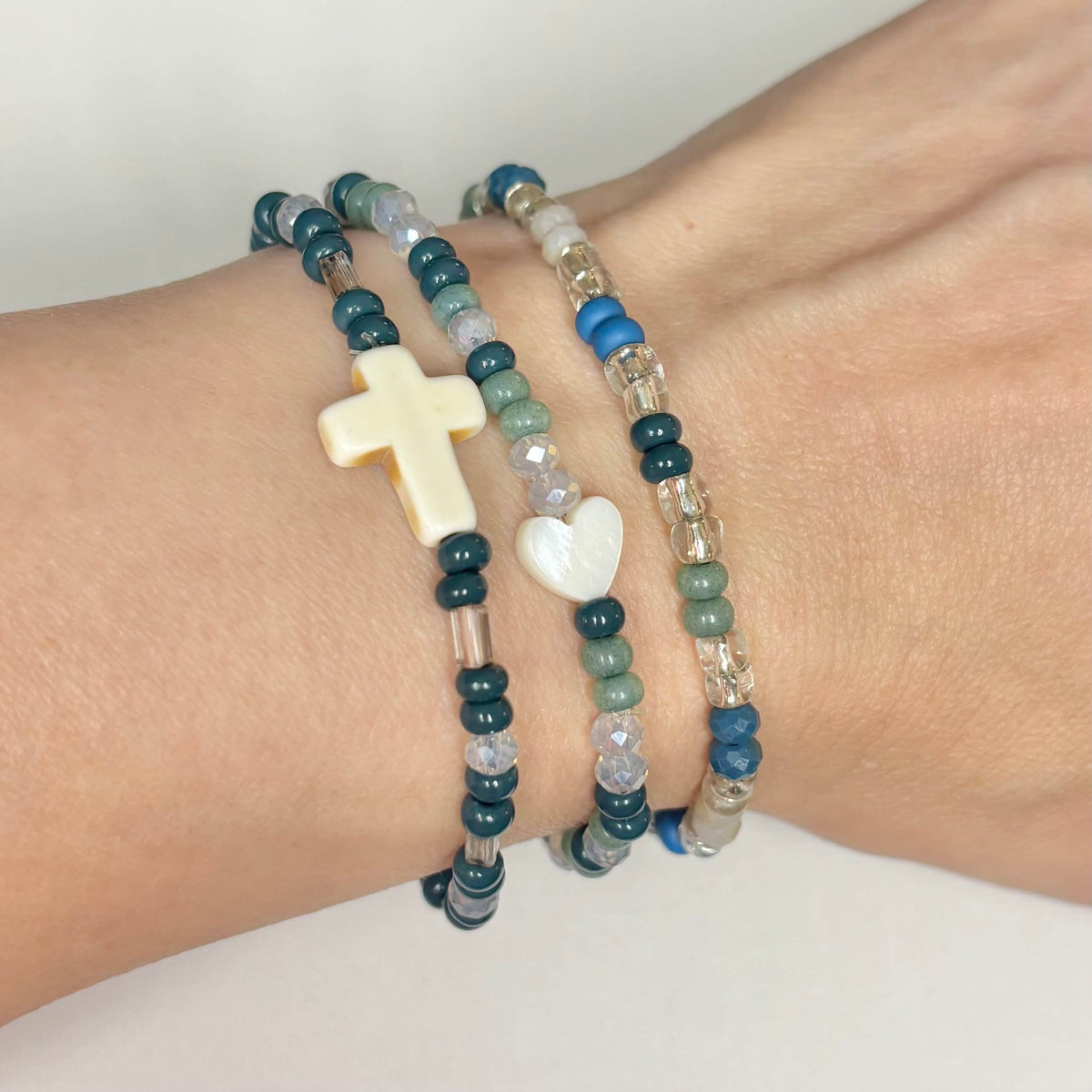 Earthy handmade 3-piece seed bead bracelet stack with shell heart and shell cross shown on wrist.