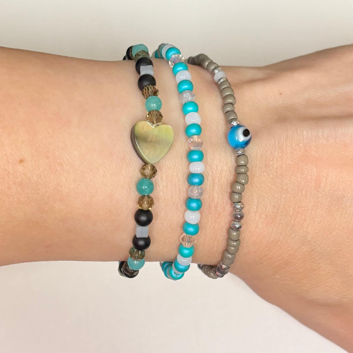 Turquoise evil eye beaded bracelet stack with mother-of-pearl heart worn on wrist.