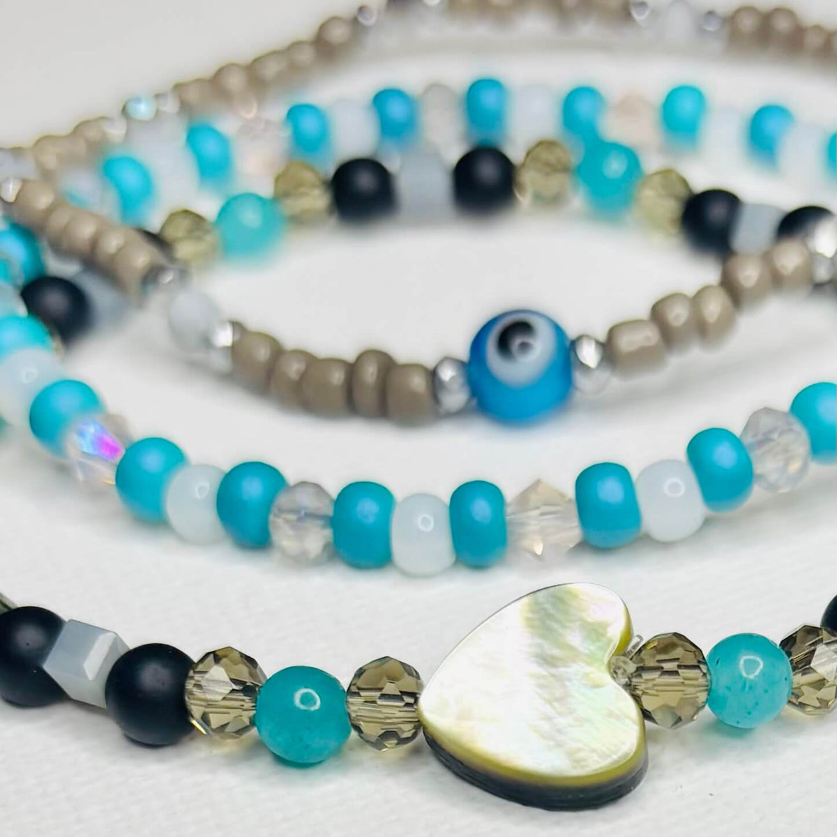 Close-up of evil eye bracelet and mother-of-pearl heart bracelet with turquoise and gray beads.