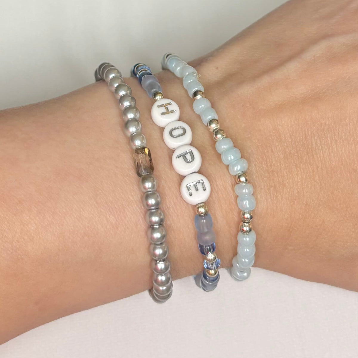 Three-piece blue and silver Hope bracelet stack with glass beads and HOPE letter beads worn on wrist.