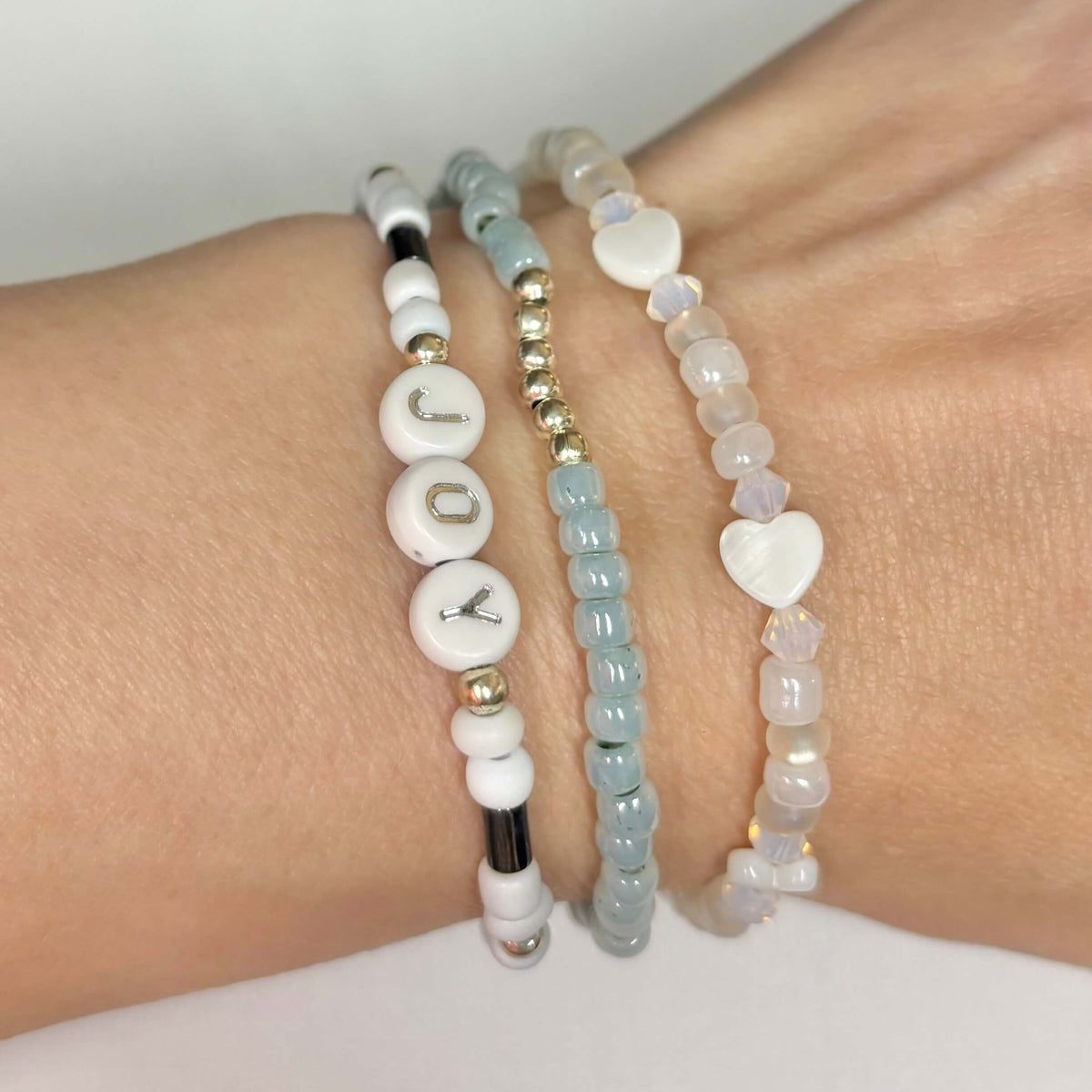 Three-piece Joy bracelet stack with blue and white beads, silver accents and shell hearts worn on wrist.