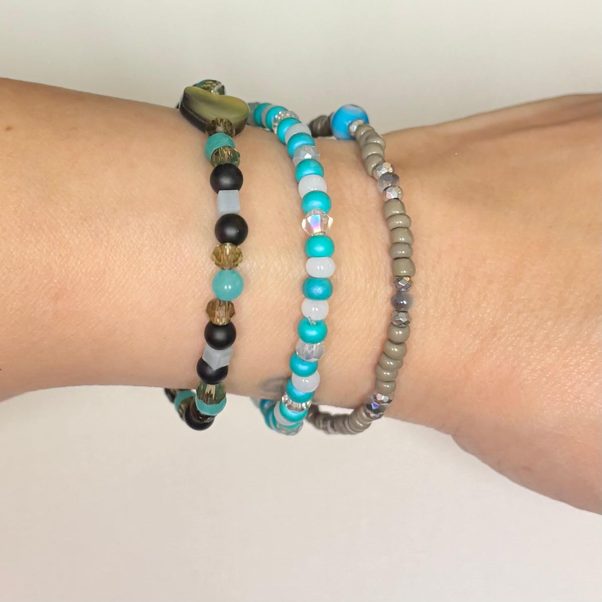 Three-piece turquoise, black and gray beaded bracelet stack worn on wrist.