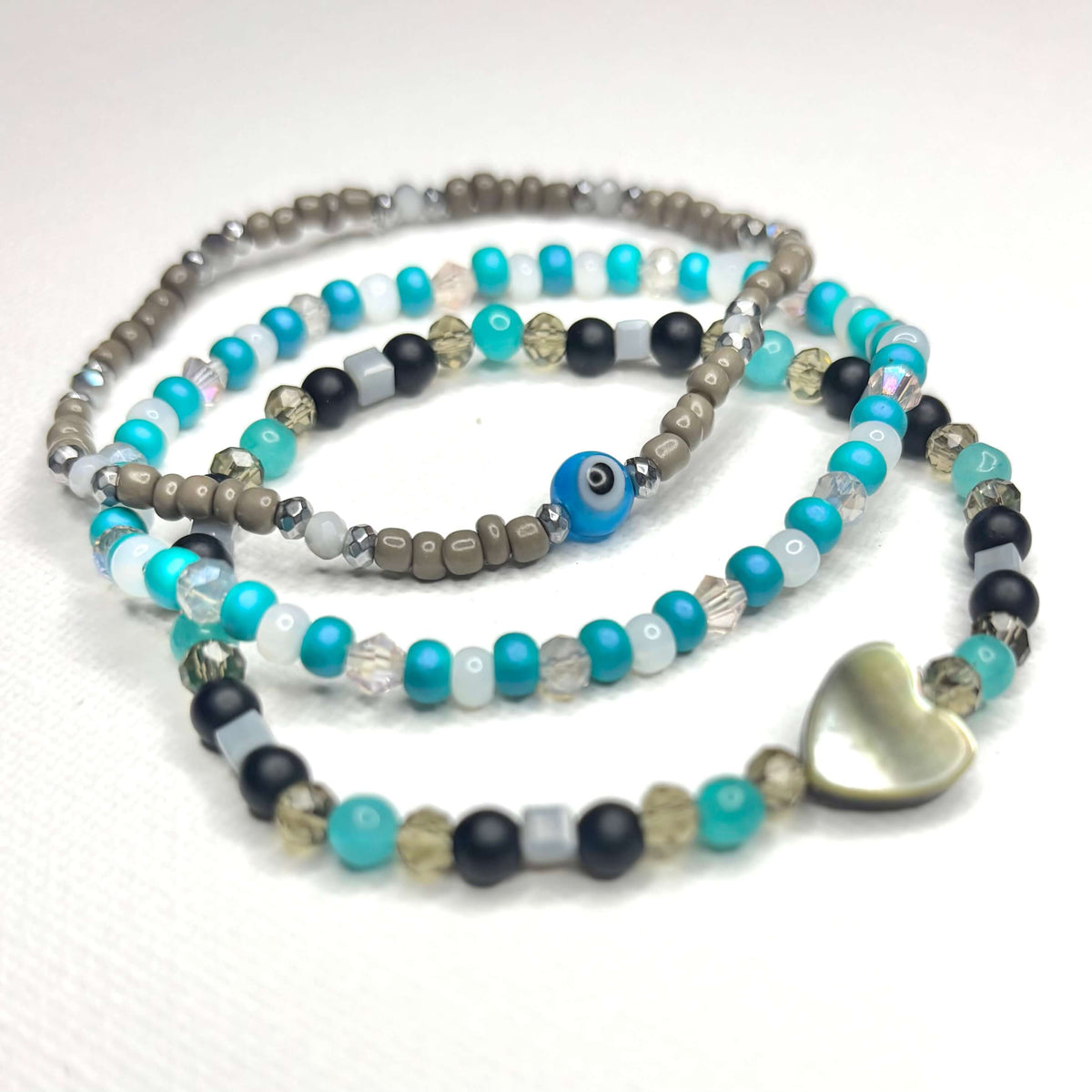 Close-up of turquoise bracelet stack with mother-of-pearl heart, black beads and evil eye.